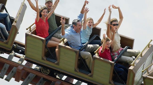 a close up of people sat in a rollercoaster with arms in the air