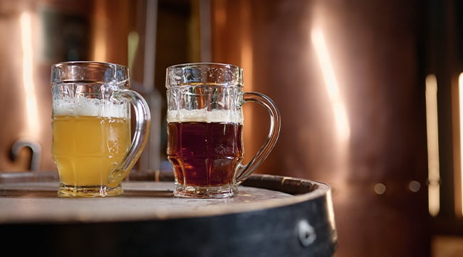 2 alcoholic drinks on top of a barrel inside a brewery