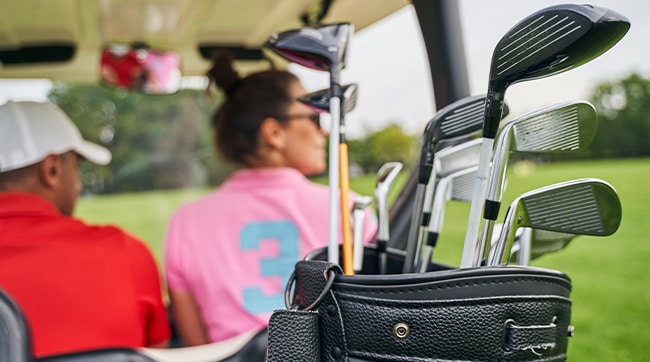 A rear view of a golf cart with bag of golf clubs and 2 golfers
