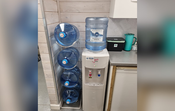 A floor standing Jazz 1100 hot and cold water cooler with bottle holder inside an office ktchen