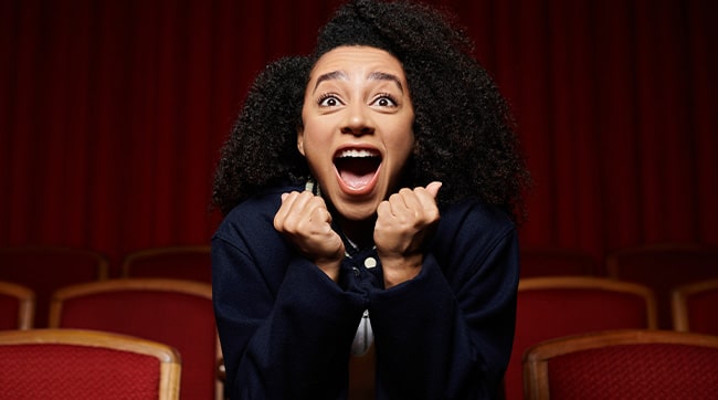 A close up of an excited woman sat in a theatre